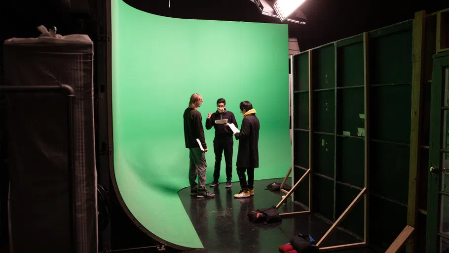 In a green-screen environment, two students rehearse lines with a director.