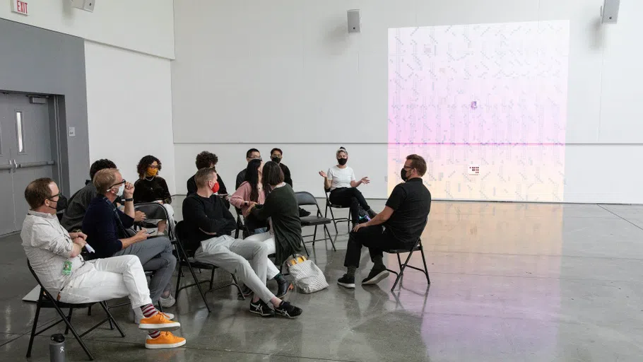 A group of Master’s Architecture students and faculty in the Nave Presentation Space with a projected work behind them.