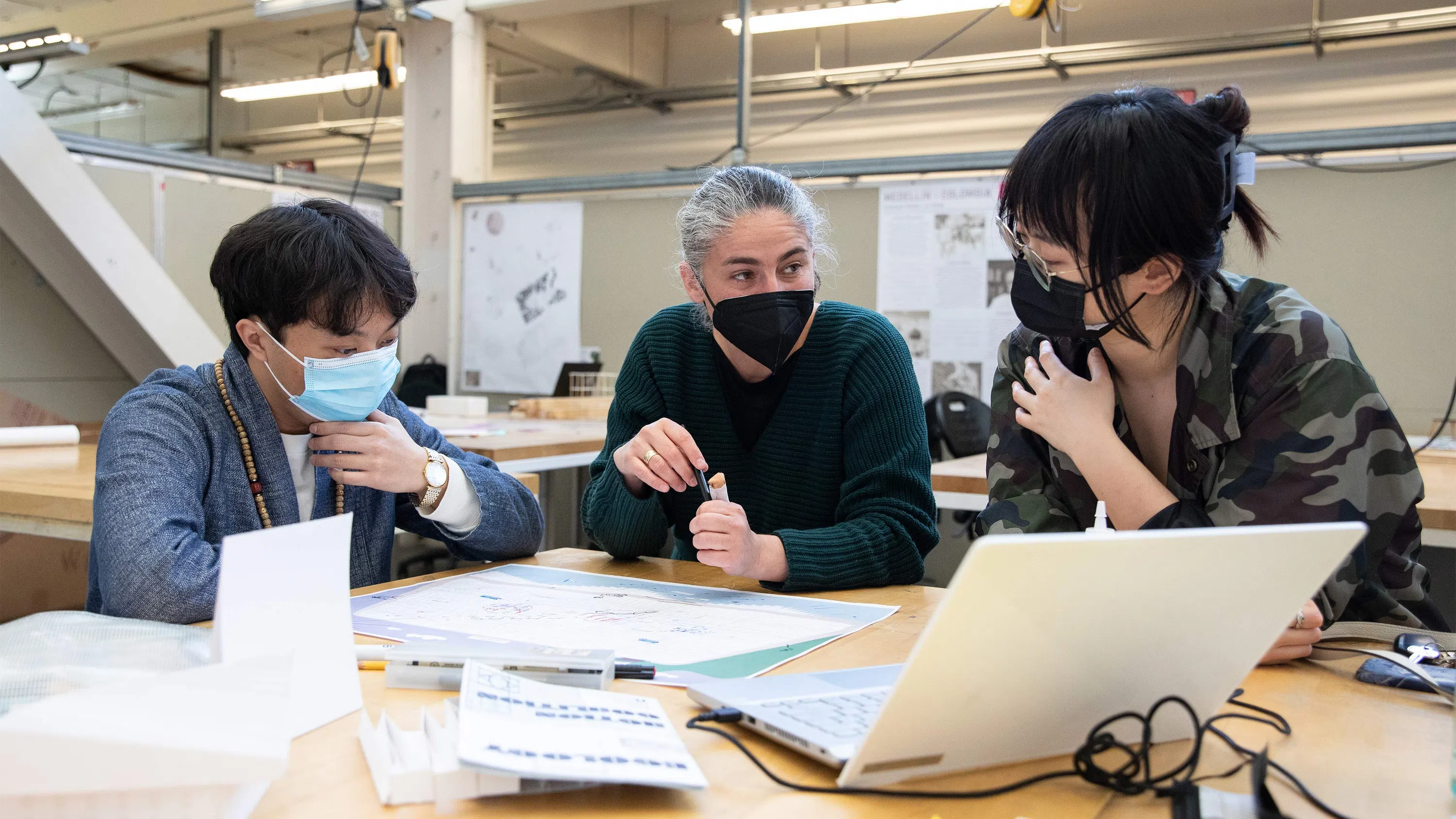 Two students look at an architectural drawing with a faculty member.