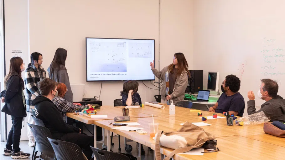 Students in front of a classroom point to a screen. 