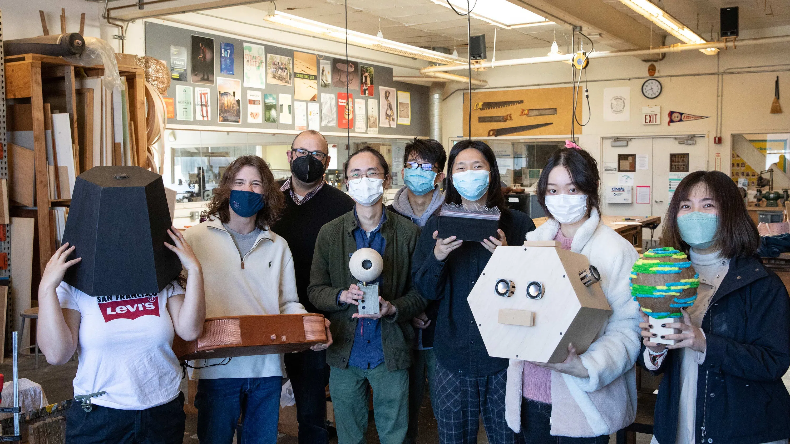 A group of students and faculty member Corey Jones display their bluetooth speaker projects in their hands—and even one on their head—in the Bench Room.