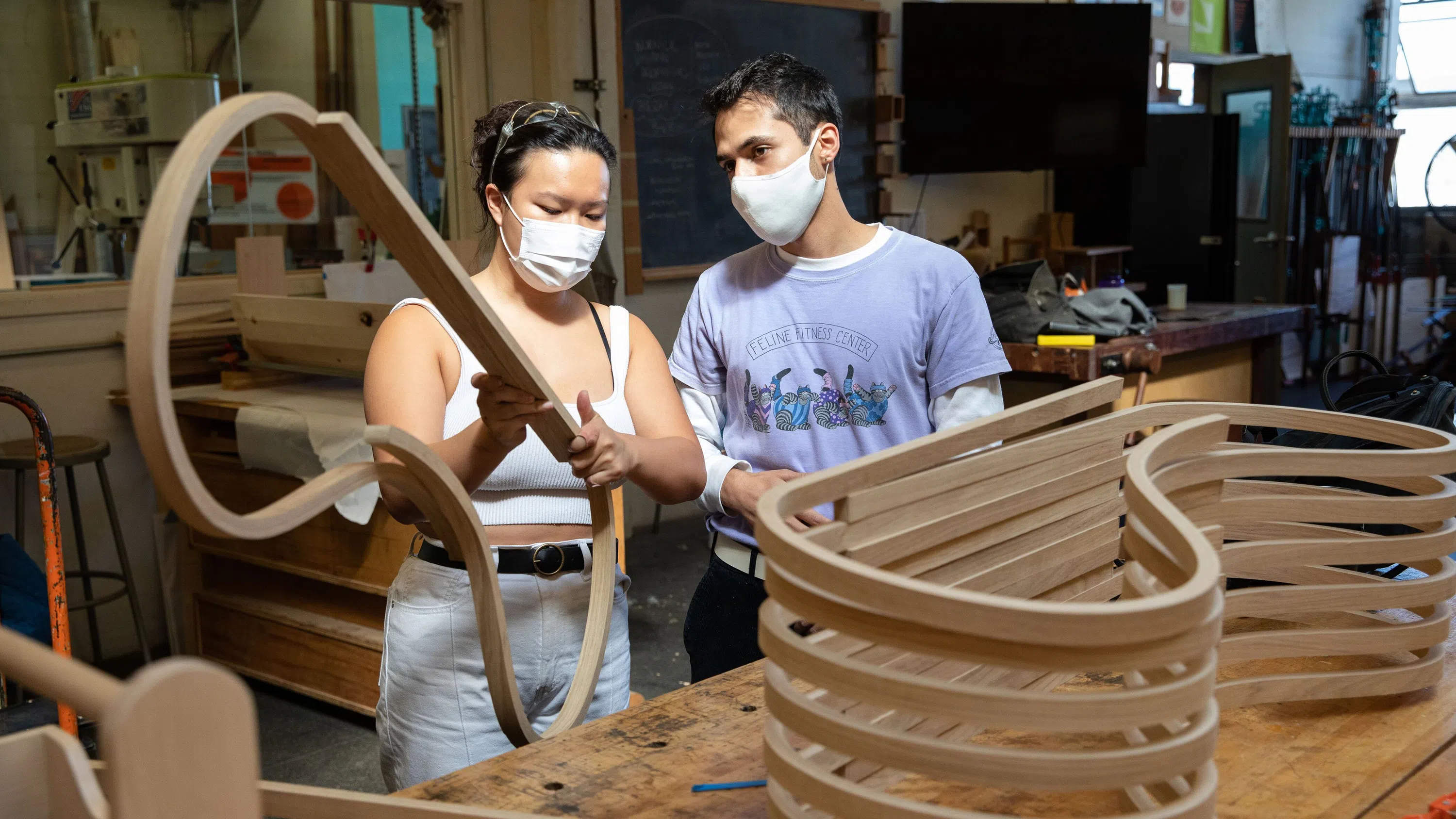 A student shows a curved wood structure to a fellow student.