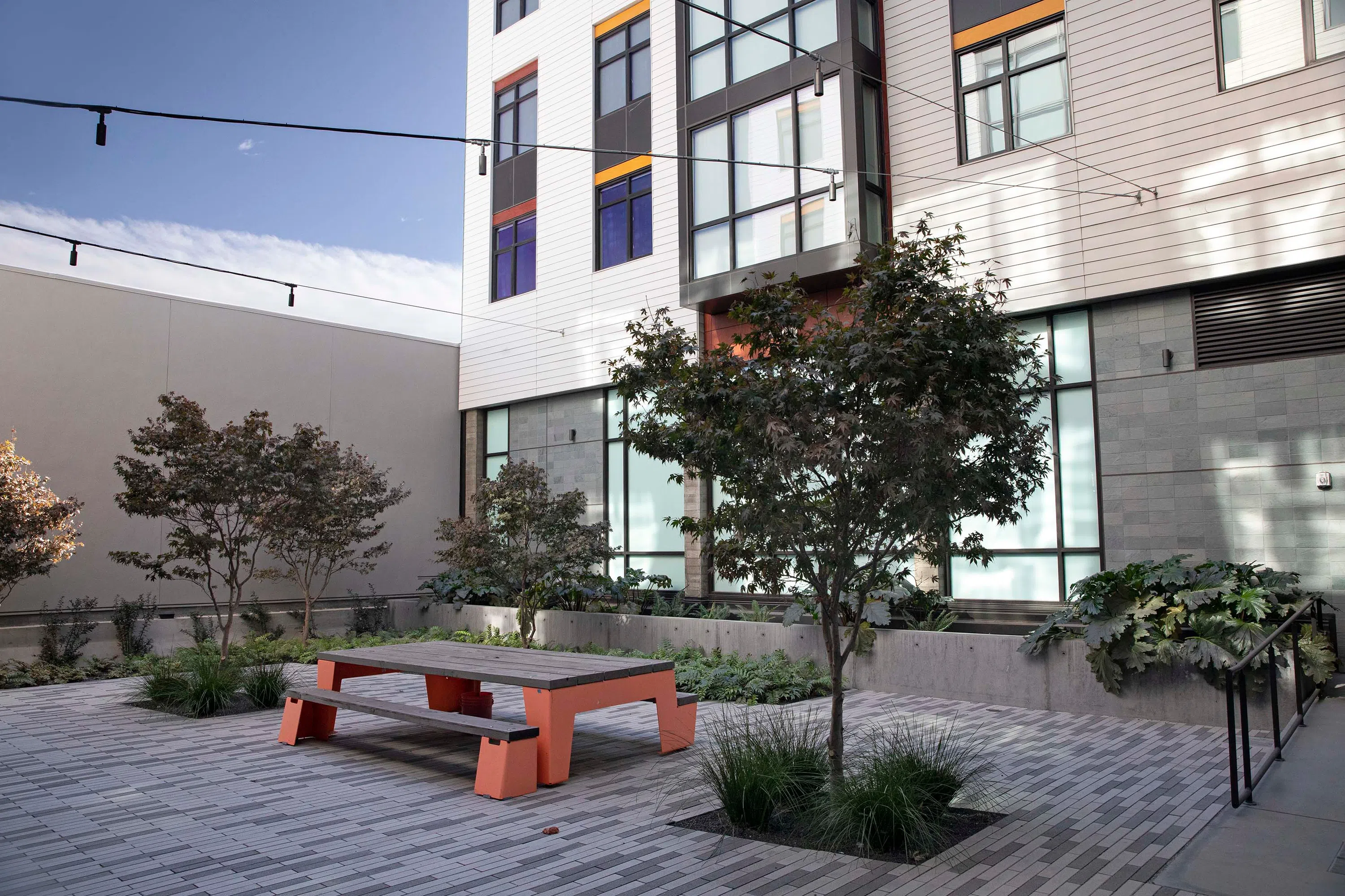 An exterior view of the interior courtyard that includes orange-and-wood tables and benches and greenery.