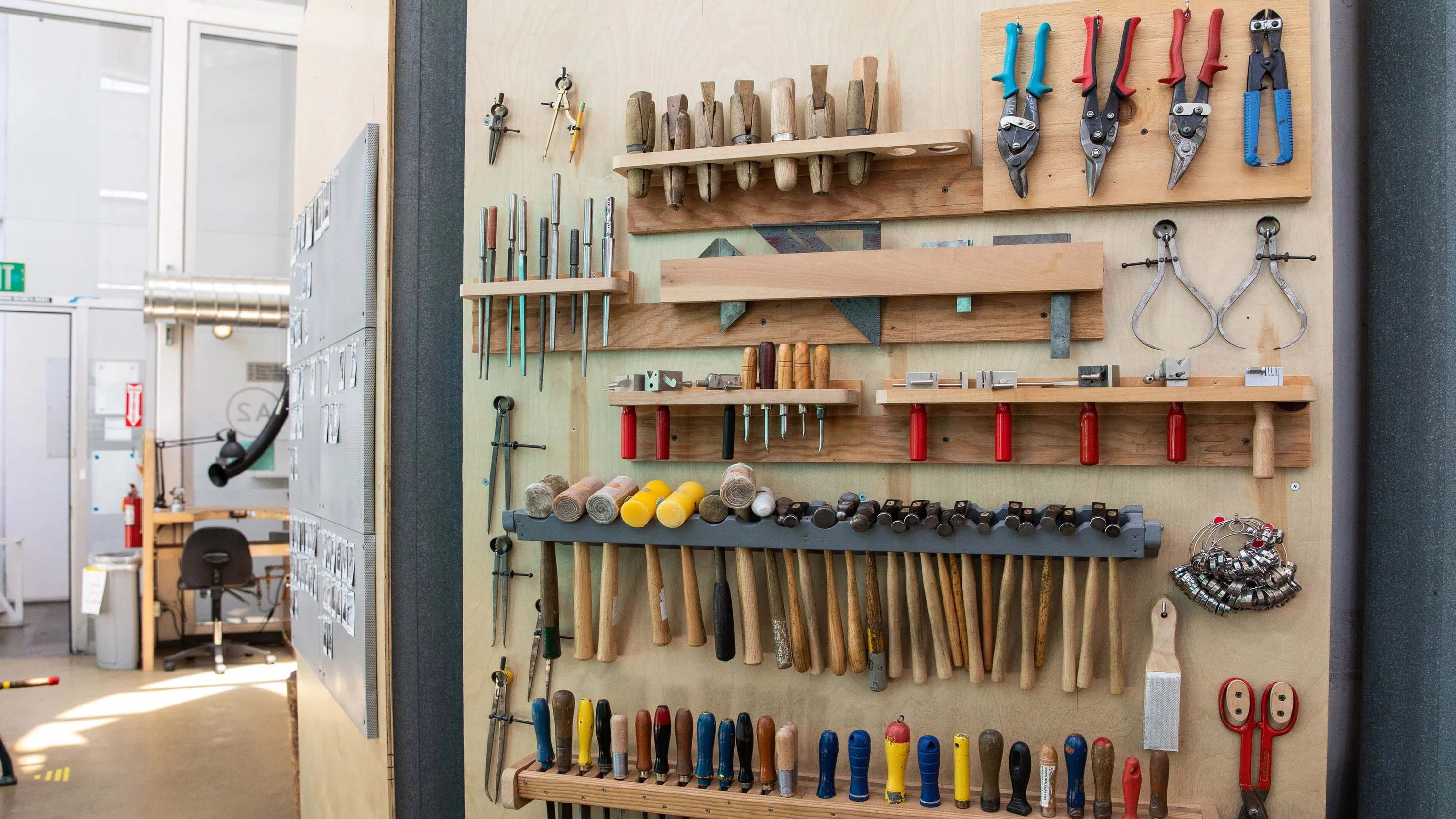 A wall lined with hammers, pliers, and other tools for metal smithing.