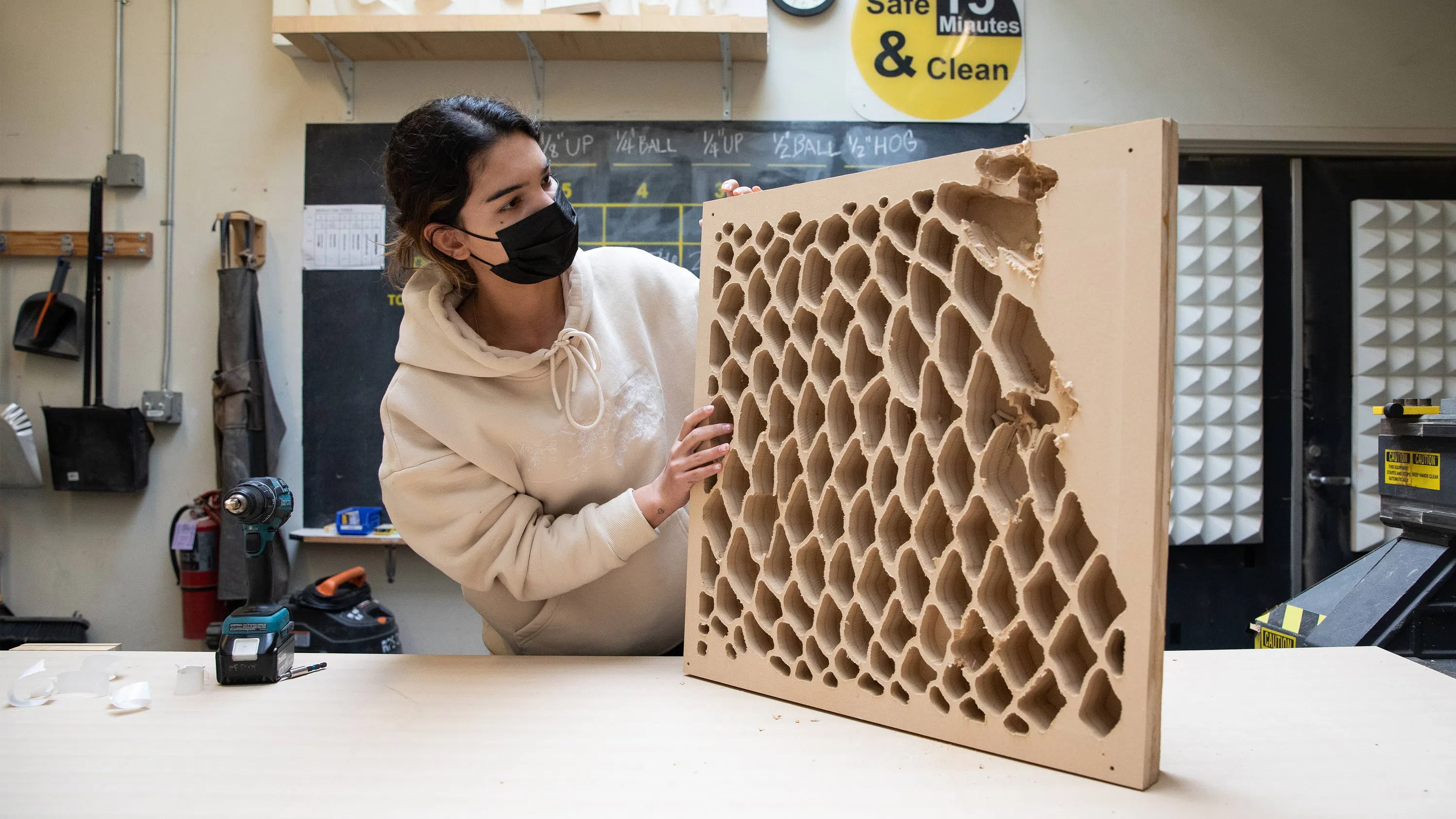 A student holds up a large piece of wood with diagonal patterns cut out.