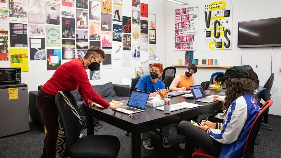 A group of writing students collaborate around a table in a space decorated with colorful posters.