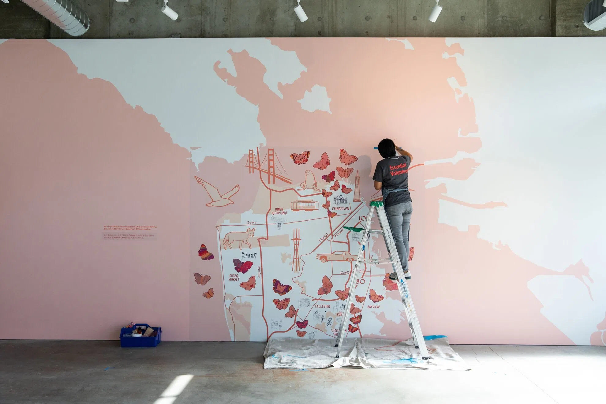 Christine Wong Yap stands on a ladder painting a large-scale mural of San Francisco. 