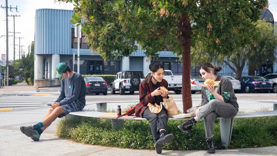 Three students eat outside of Makers Cafe with 80 Carolina in the background.