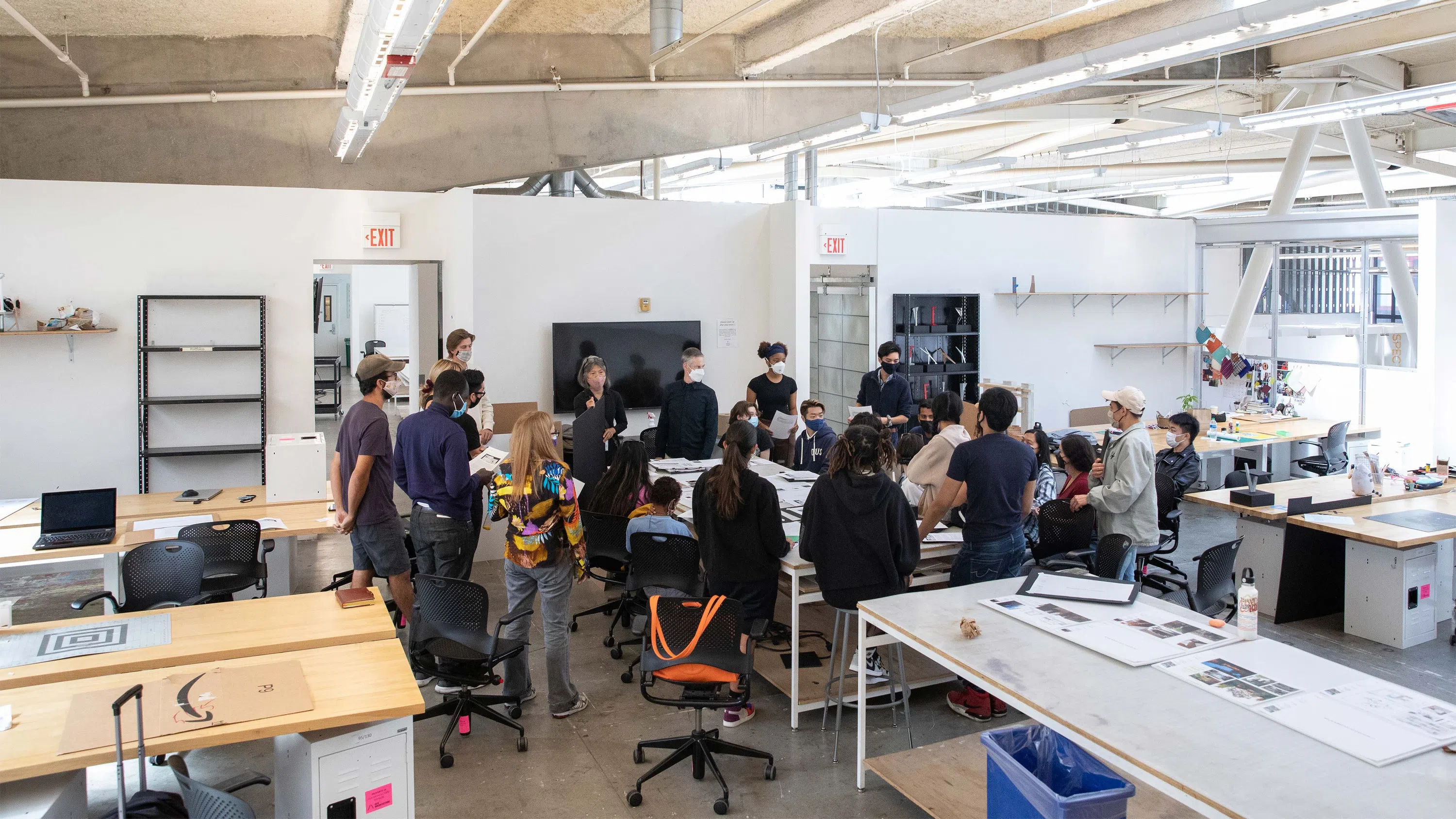 A wide shot of students clustered around faculty Margaret Ikeda and Mark Donahue in the architecture studios.