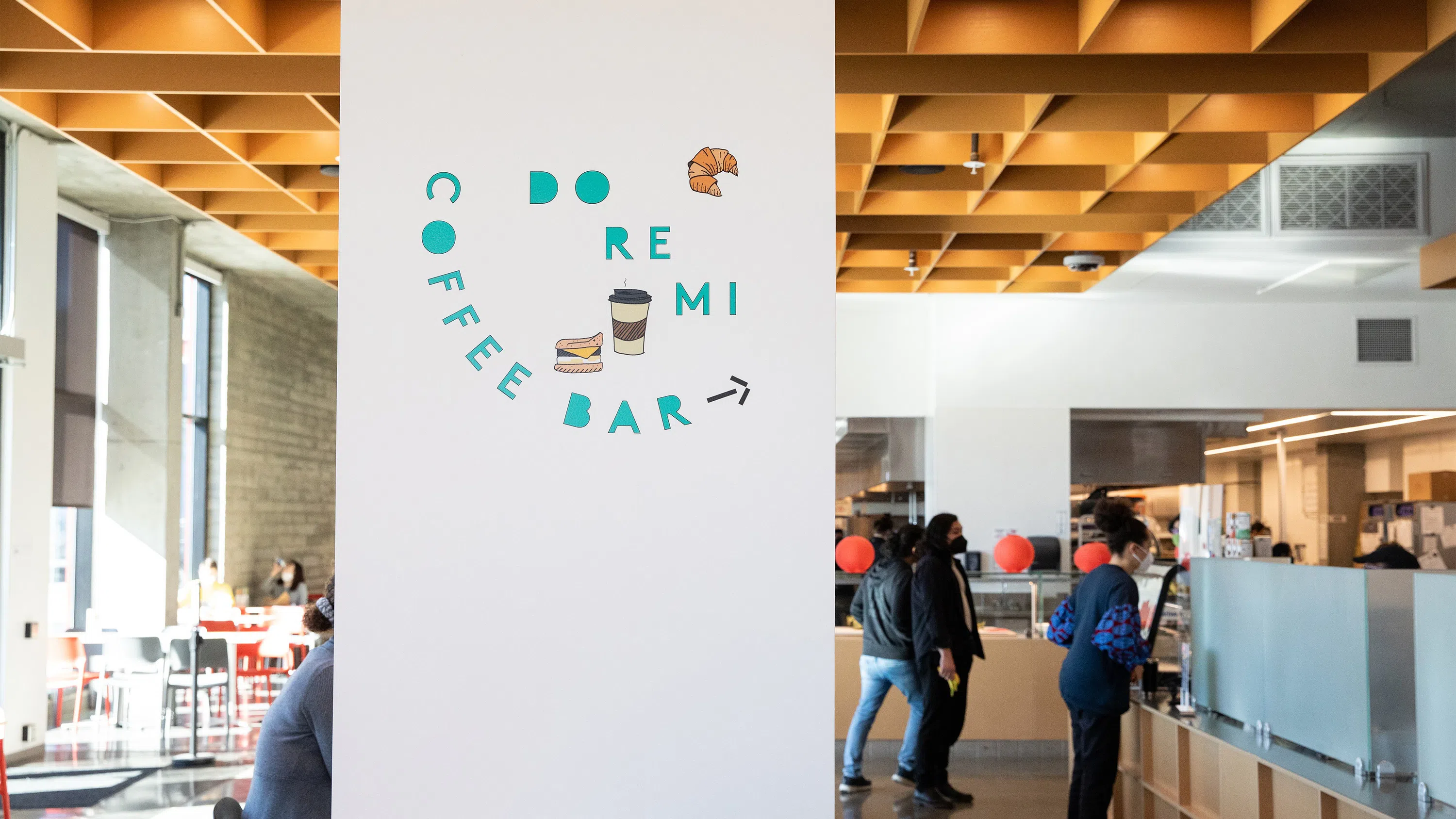 A few people order coffee at a counter. A pillar in the center of the frame reads DoReMi Coffee bar in teal vinyl.