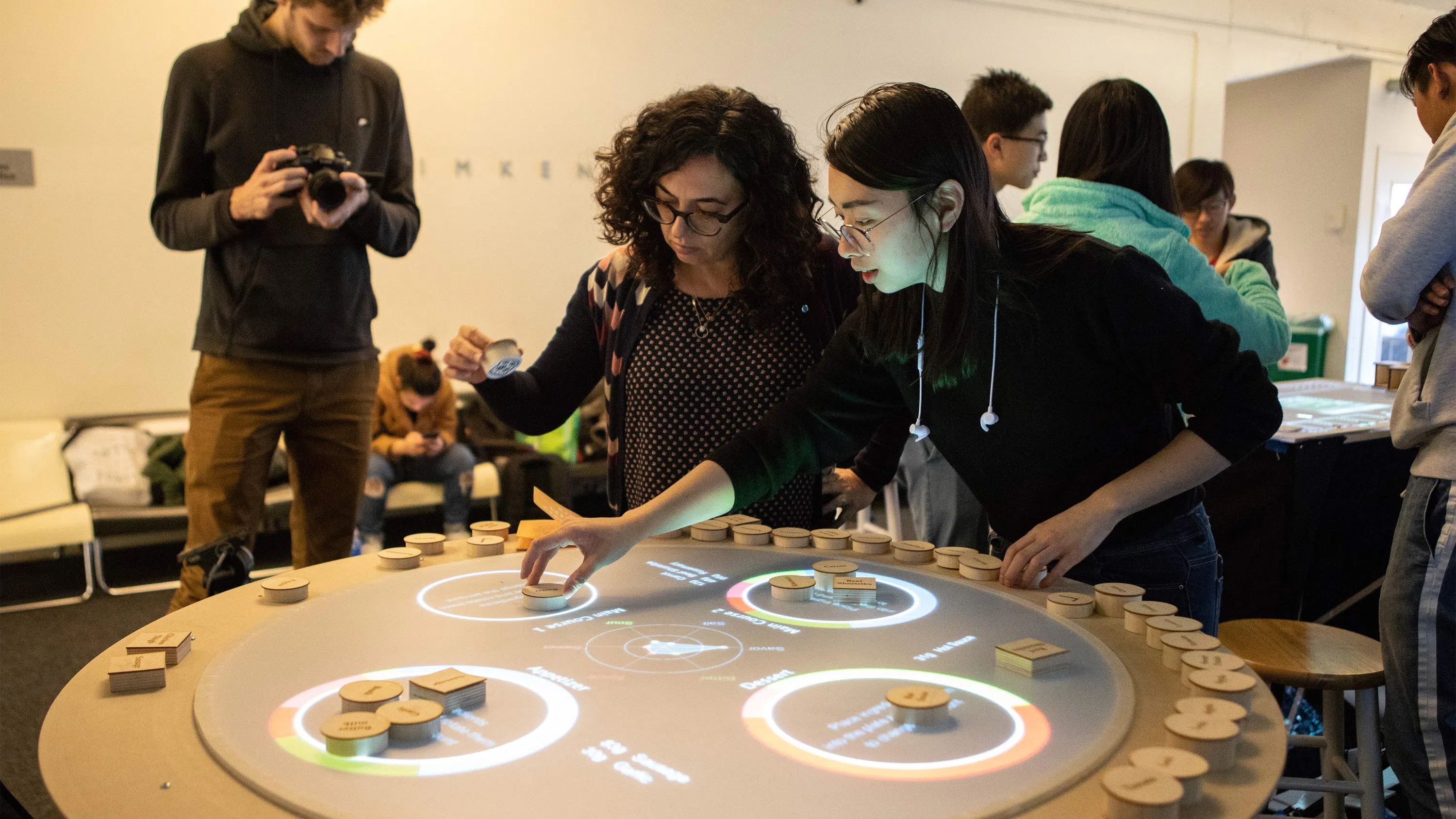 Dean Helen Maria and a student interact with wooden objects on a LED-lit table.