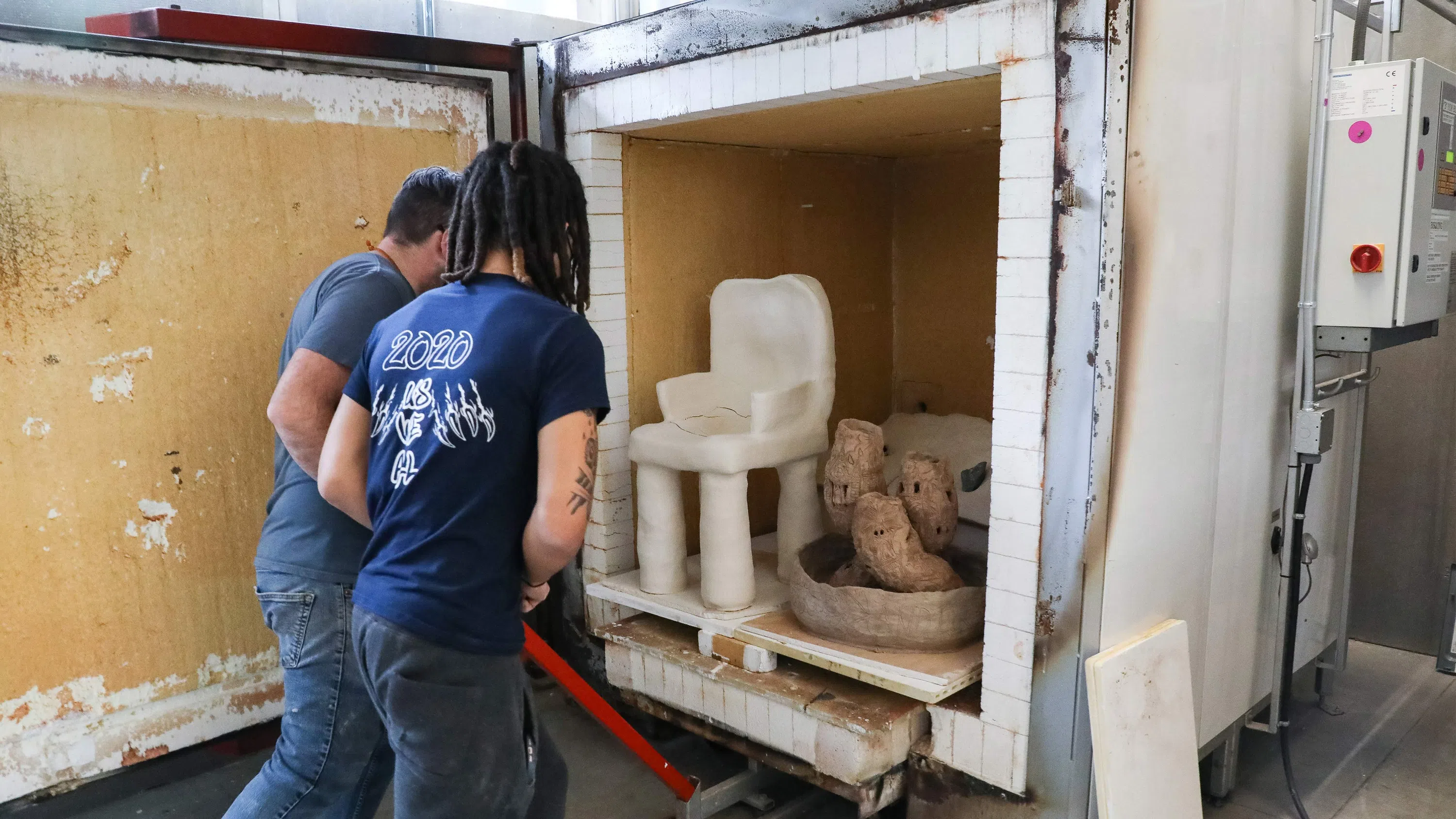 Two men load artwork into a kiln. 