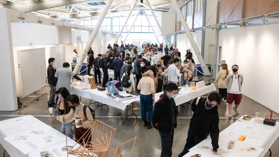 Architecture students and faculty view models and drawings on v-shaped tables running the length of the Nave. 