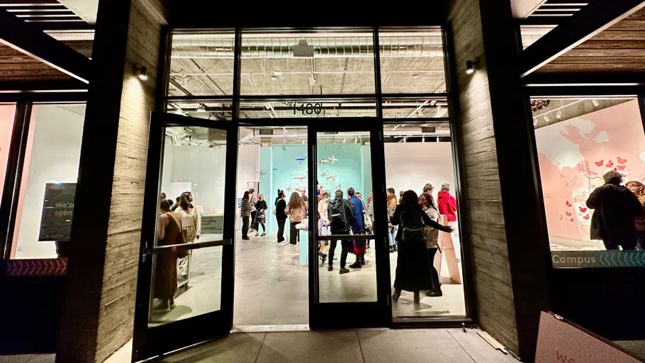 The exterior of the CCA Campus Gallery during the evening opening, with silhouetted crowd against the pastel blue and pink walls.