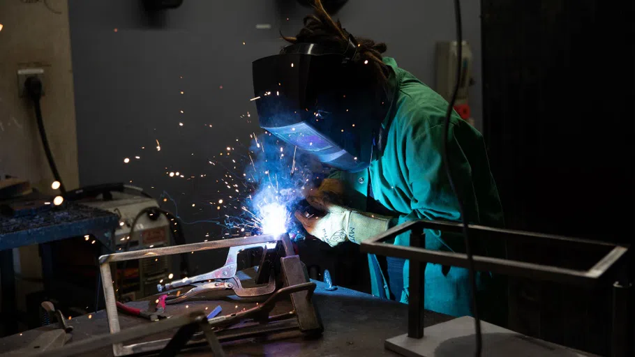 Sparks fly as Laurus Myth, in protective welding gear, fuses parts of a metal frame together.