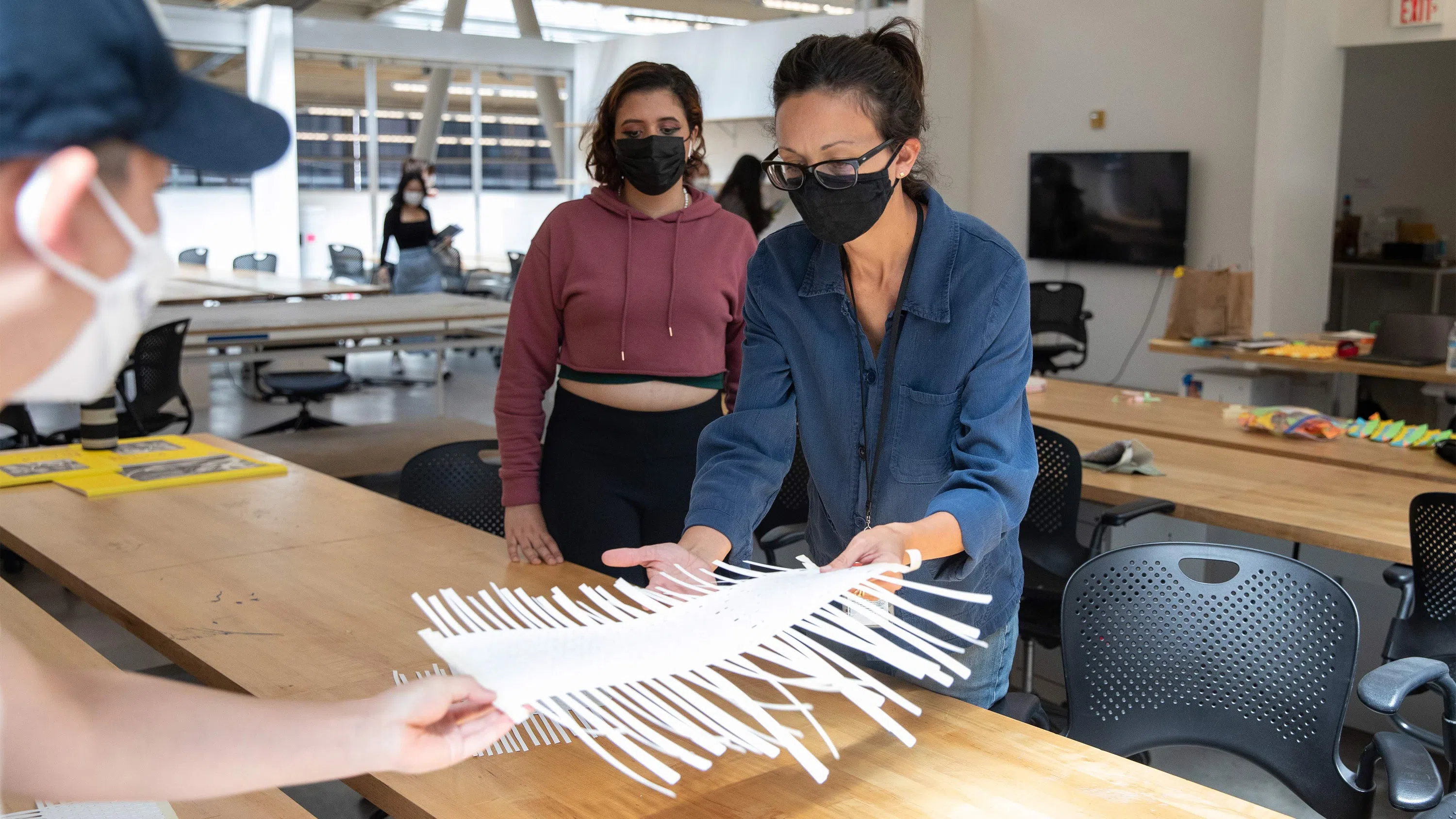 A student touches a delicate paper model held by faculty Margaux Schindler.