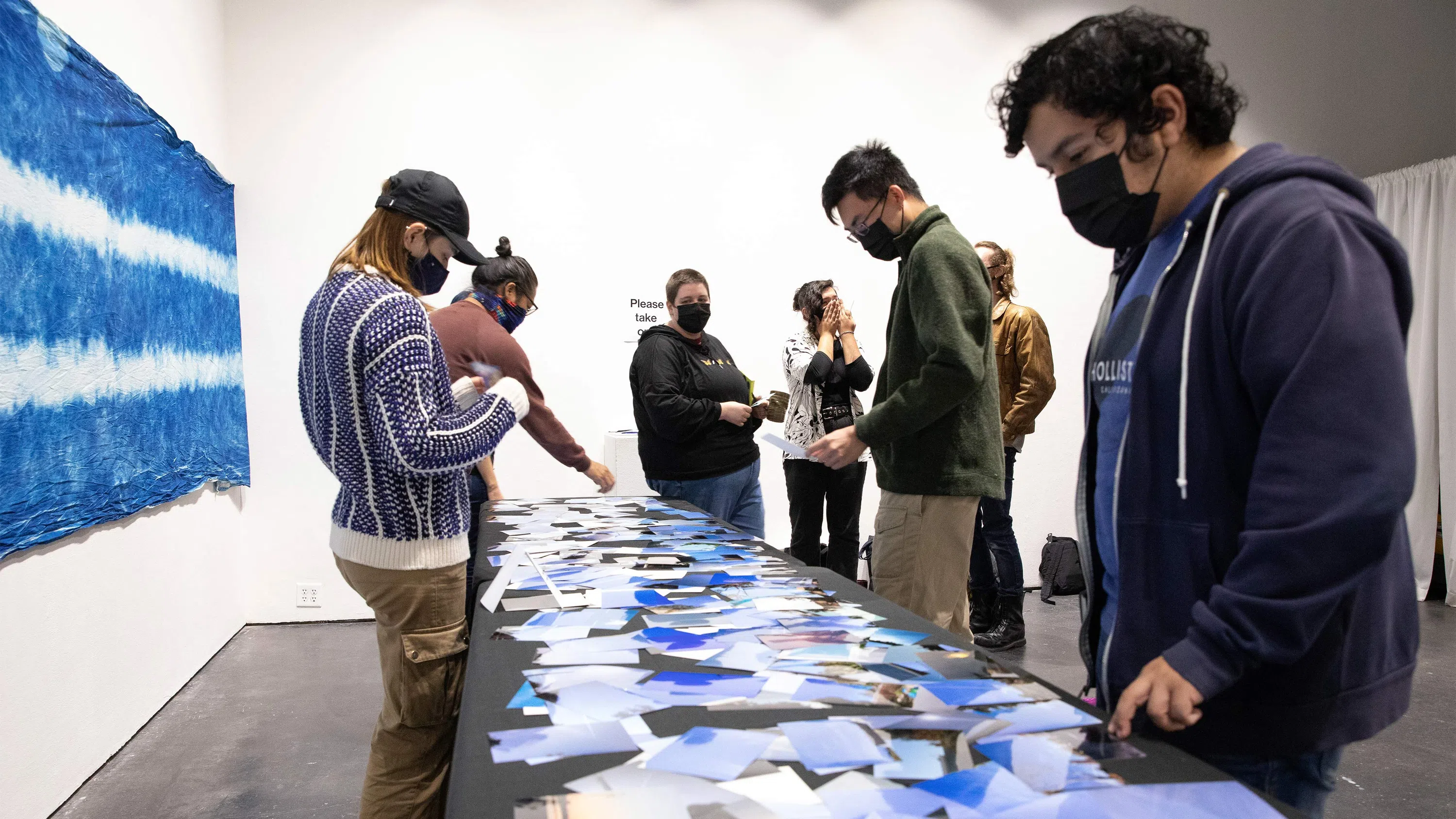Various students review small cyanotypes on a white table; a large-scale one hangs behind them on a wall.