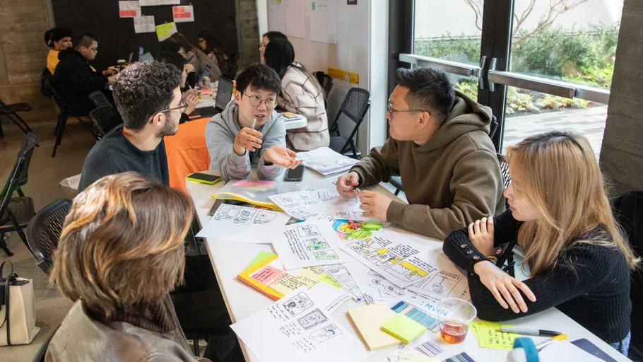 Five students sit at a table with paper and post-its.