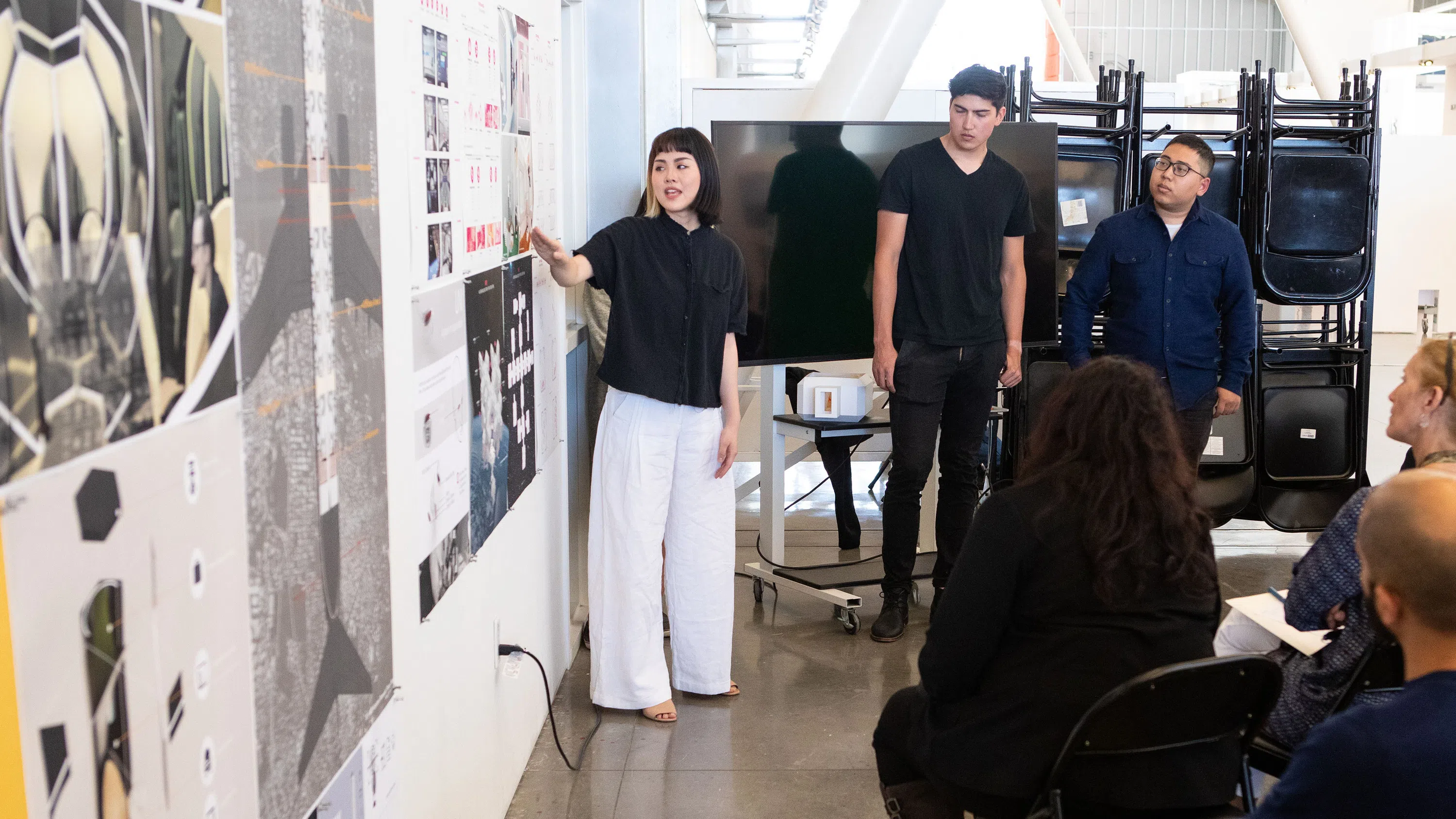A student gestures at a pin-up installation of her work during an Interior Design critique.