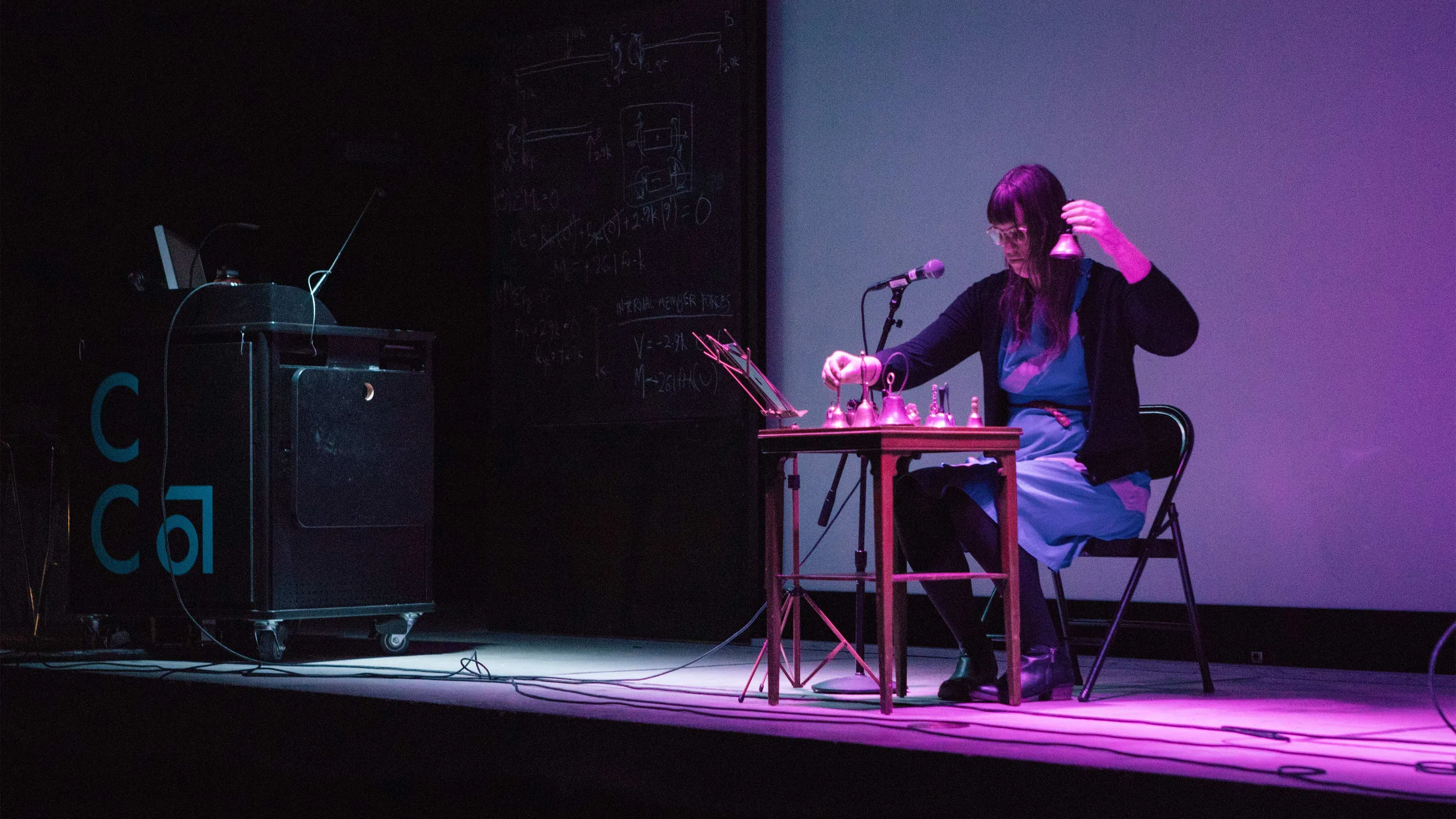 Under purple lights, a sound artist performs with chimes on stage.