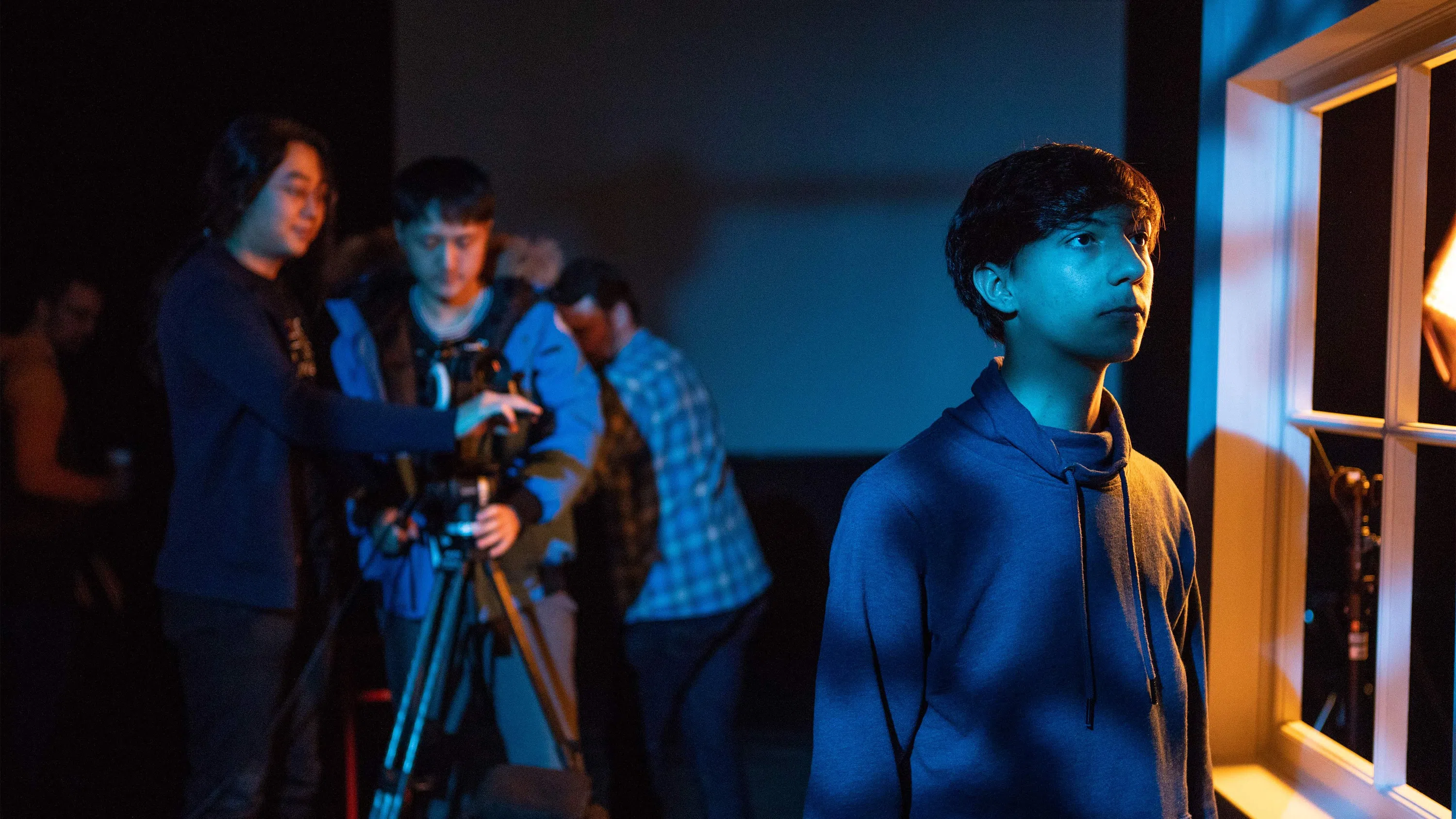Two student-cinematographers film an actor on stage in dramatic blue lighting.