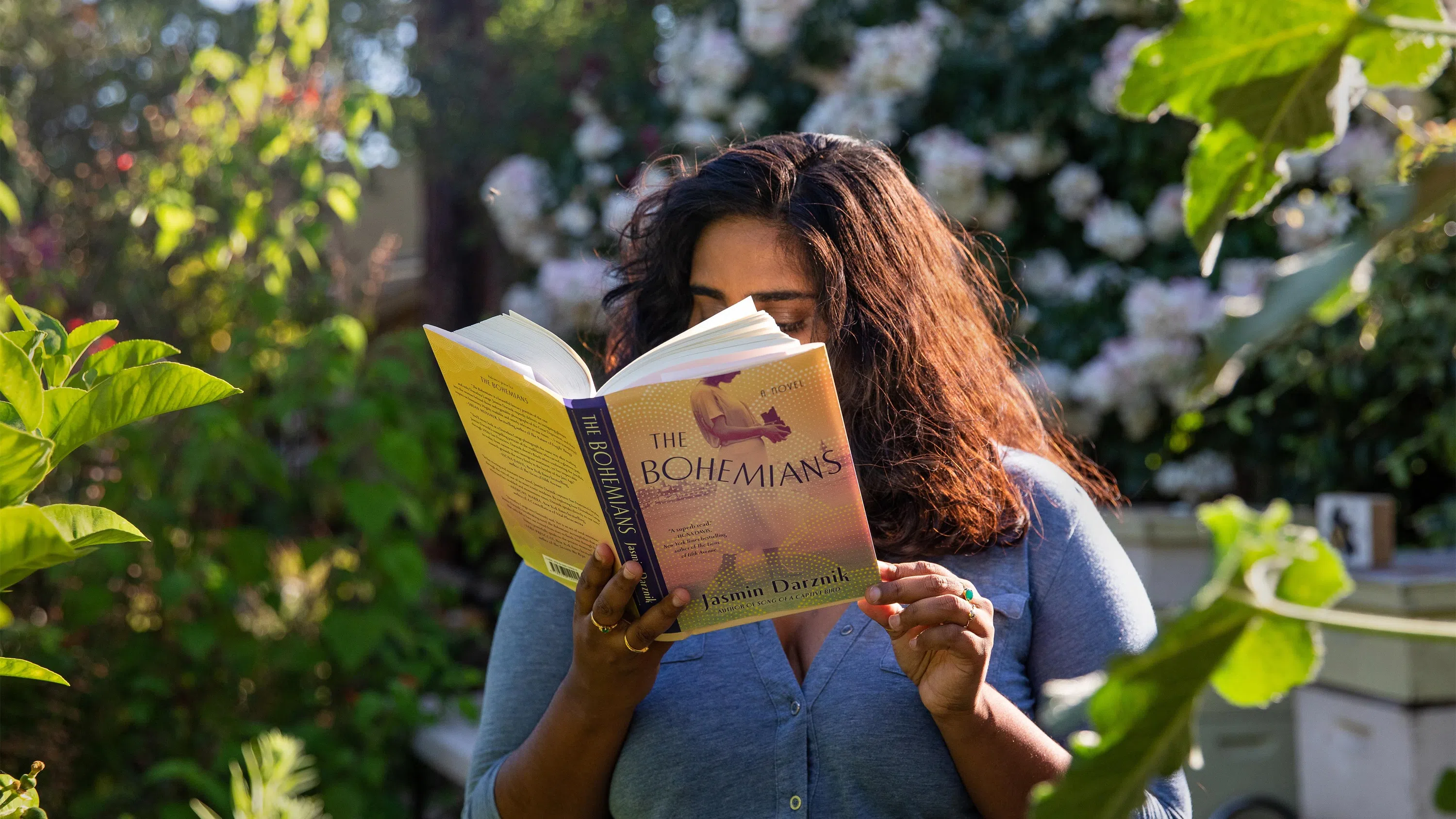A person with curly hair reads Faculty Jasmin Darznik’s book The Bohemians.