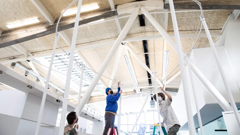 An upward-tilted shot of students Joel Lithgow and Joseph Blake constructing a gazebo-like armature in the Nave.