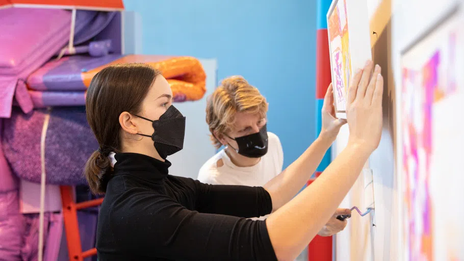 Two students paint and install artwork in a gallery.