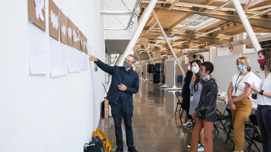 Chair Brian Price points at work pinned to the wall while the class listens around him.