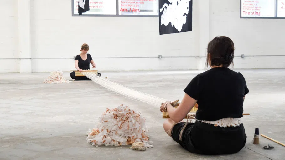 Two students sitting on the floor weaving