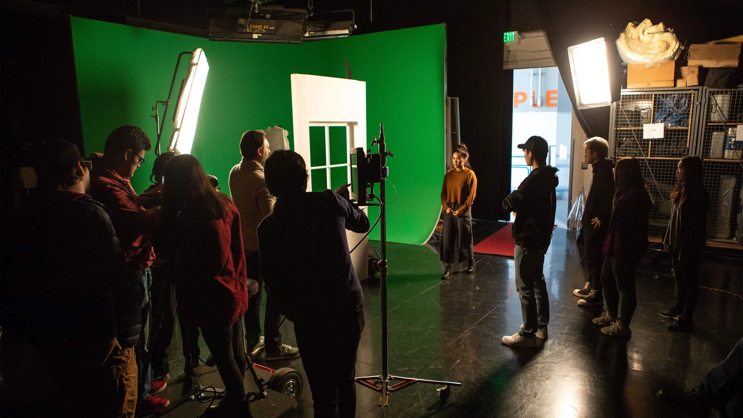 A dozen students stand on the production stage holding film equipment preparing for a shoot.