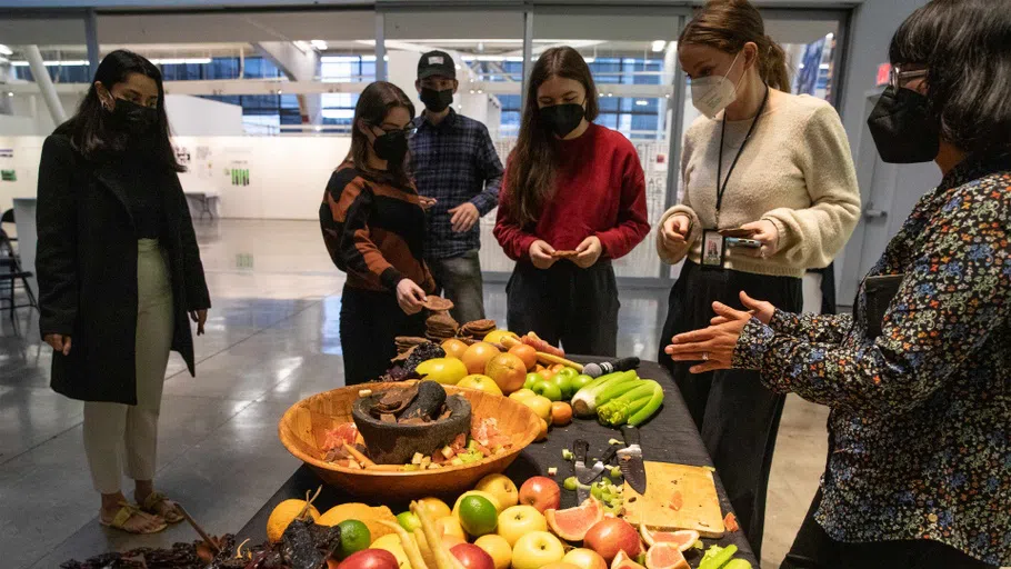 In the Nave Alcove, a small group listens to artist SiouxBean around a table with fruit, grains, and vegetables.