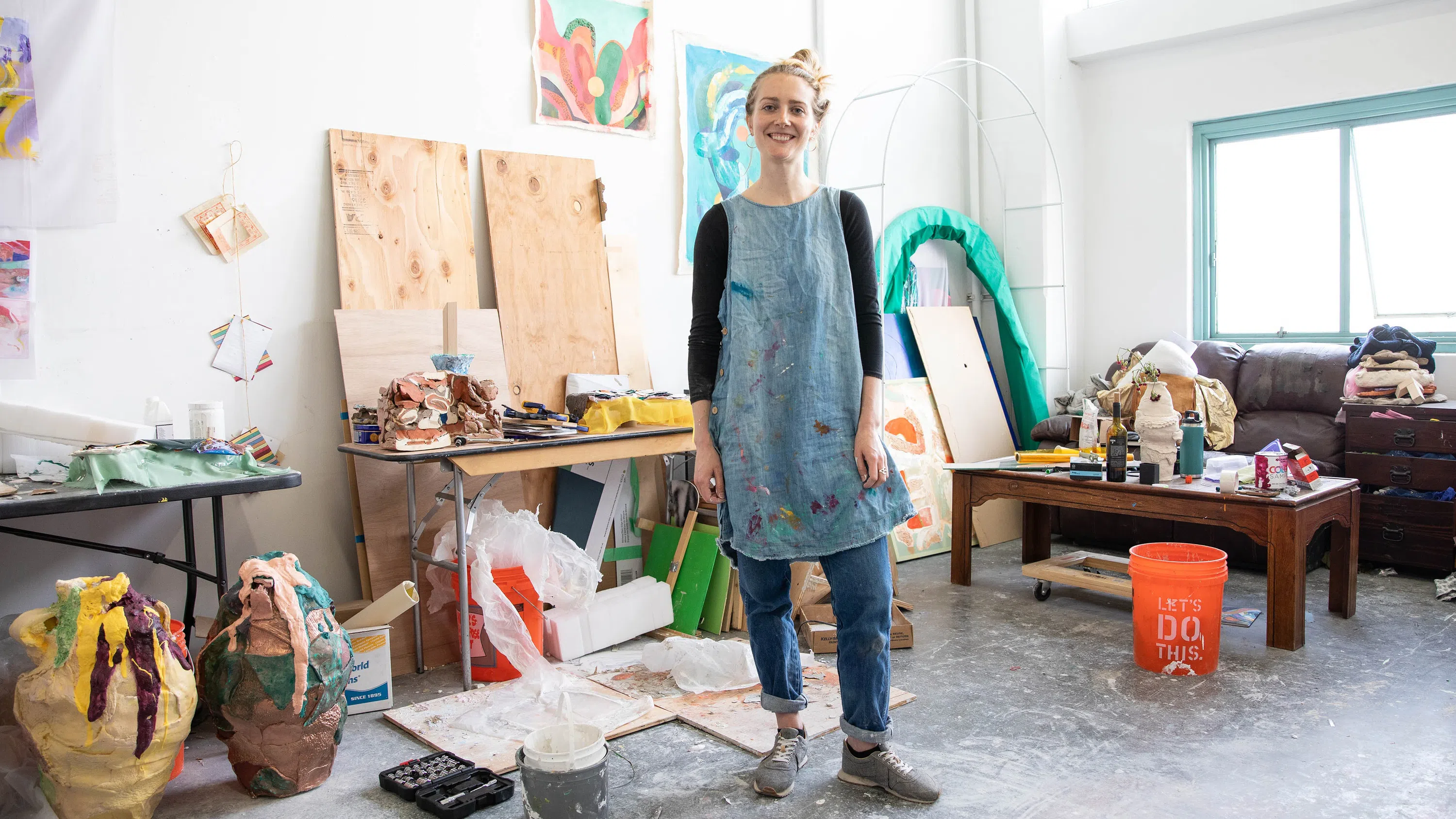  Courtney Odell stands in her studio in front of her artwork and supplies on the floor and walls. 