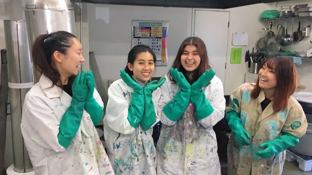 Four students in stained lab coats and teal gloves pose in a lab,