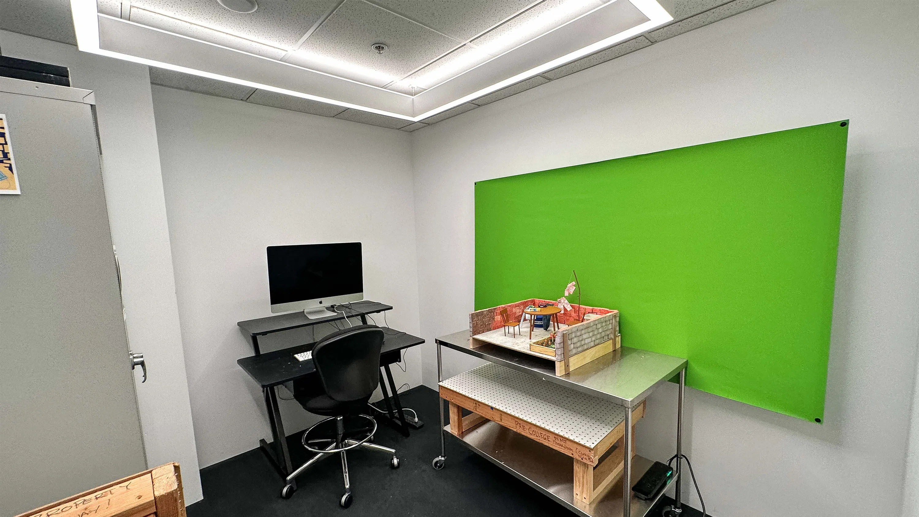 A small room with a green screen, iMac computer, and a model for a stop motion animation project. 