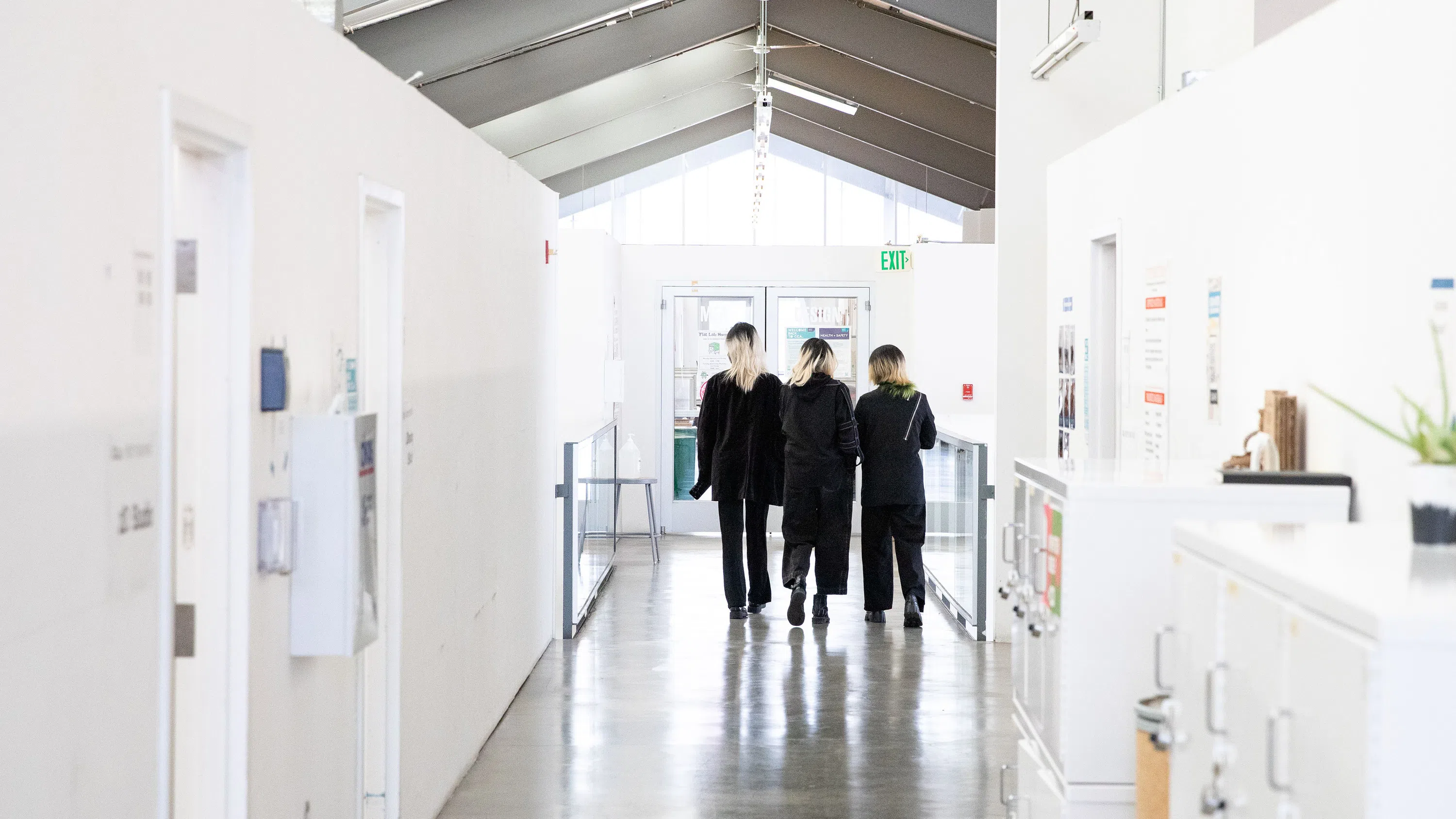 Three students dressed in black walk toward the end of a light-filled hallway. 