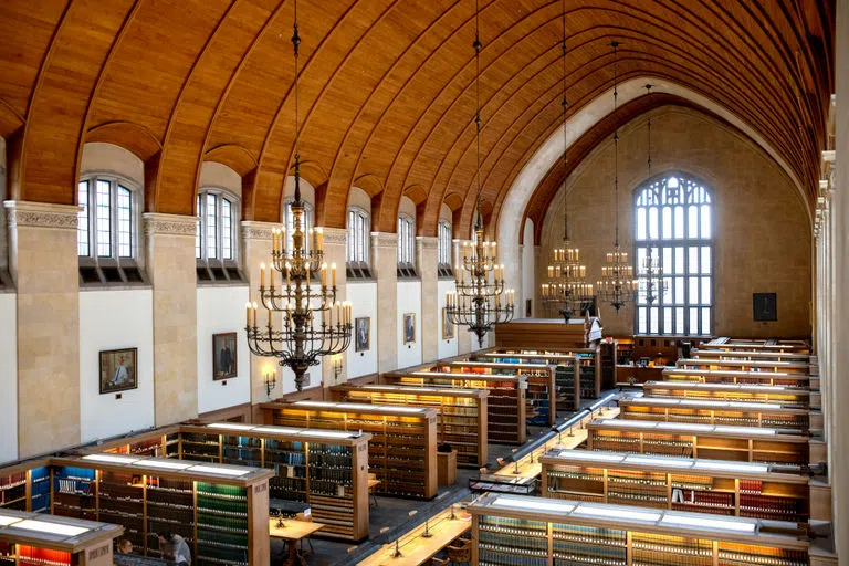 An aerial view of the study nooks between bookshelves at the Law Library at Myron Taylor Hall, with an arched wooden ceiling and chandeliers hanging above tables in a line down the center of the room. 