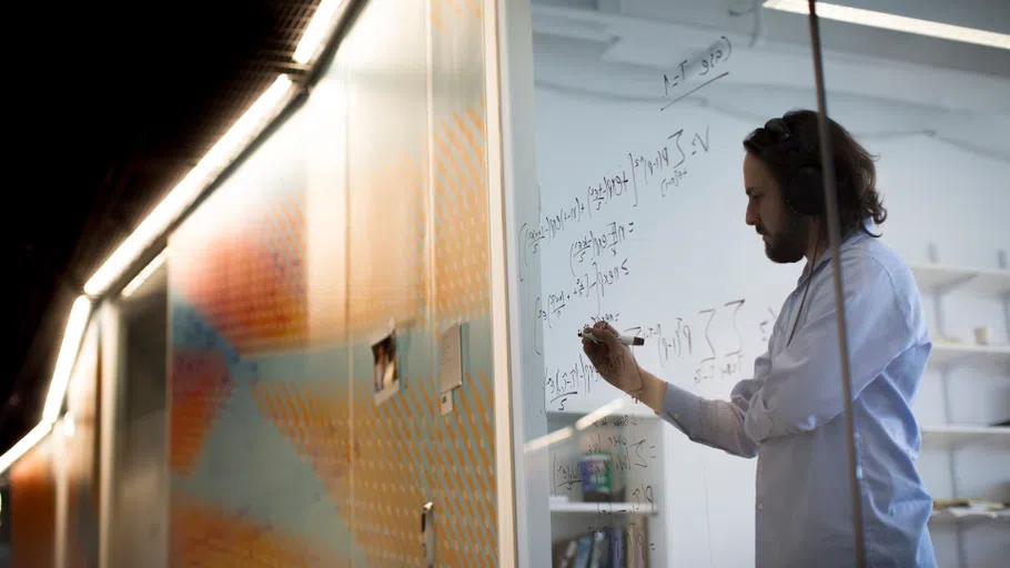 A mathematician works with formulas on a clear vertical surface.