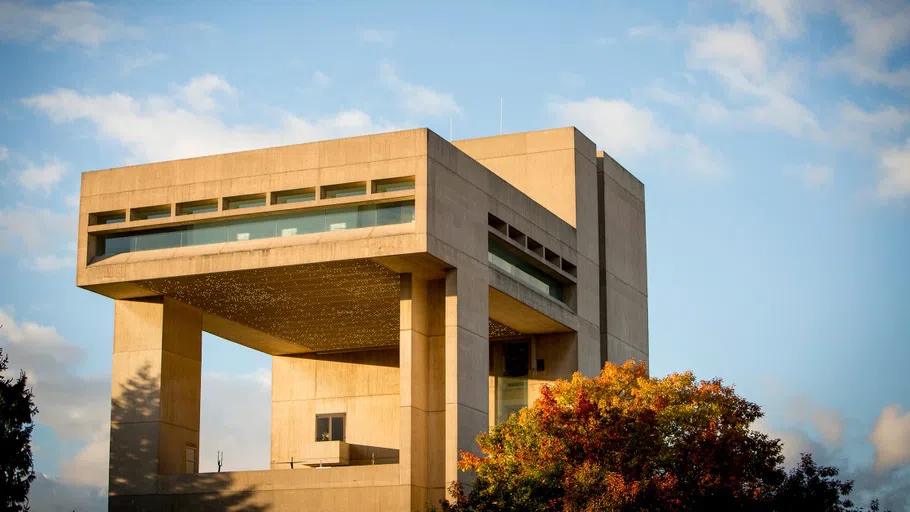 Exterior of the Herbert F. Johnson Museum of Art at Cornell University, as seen in autumn. Behind it is a blue sky with a few clouds.