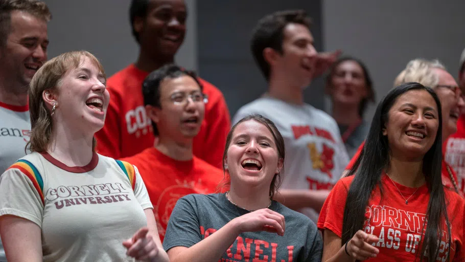 A group of eight students performing on stage. They are each wearing Cornell T-shirts of varying colors and designs.