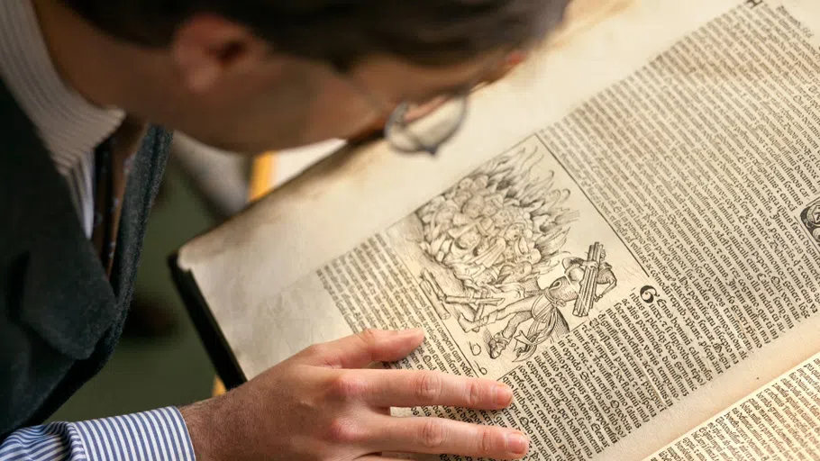 A person, seen from overhead, looks at a rare book from the Cornell Library’s Rare and Manuscript Collections.