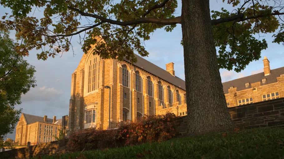 Exterior of Willard Straight Hall. In the foreground is a grassy hill and some trees.