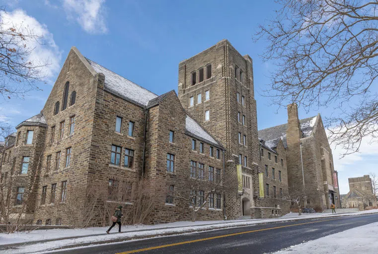 The exterior of Myron Taylor Hall with a blue sky above and a student walking on the snowy sidewalk in front of the building.