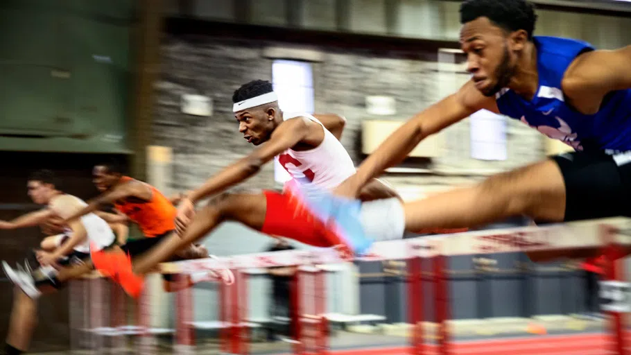 Several runners jump over hurdles on the track inside Barton Hall.