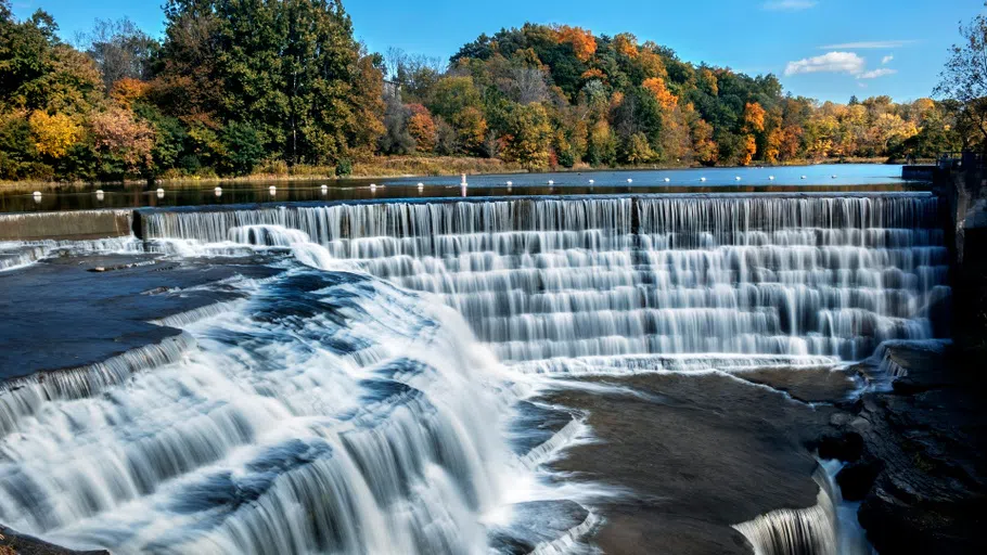 Triphammer Falls cascades down from Beebe Lake surrounded by colorful autumn leaves.