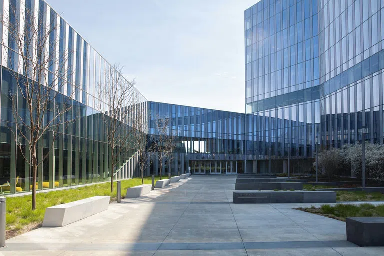 A courtyard lined with trees, concrete benches and gardens, leads to the entrance of CVM Center, a building made up of glass windows from top to bottom.