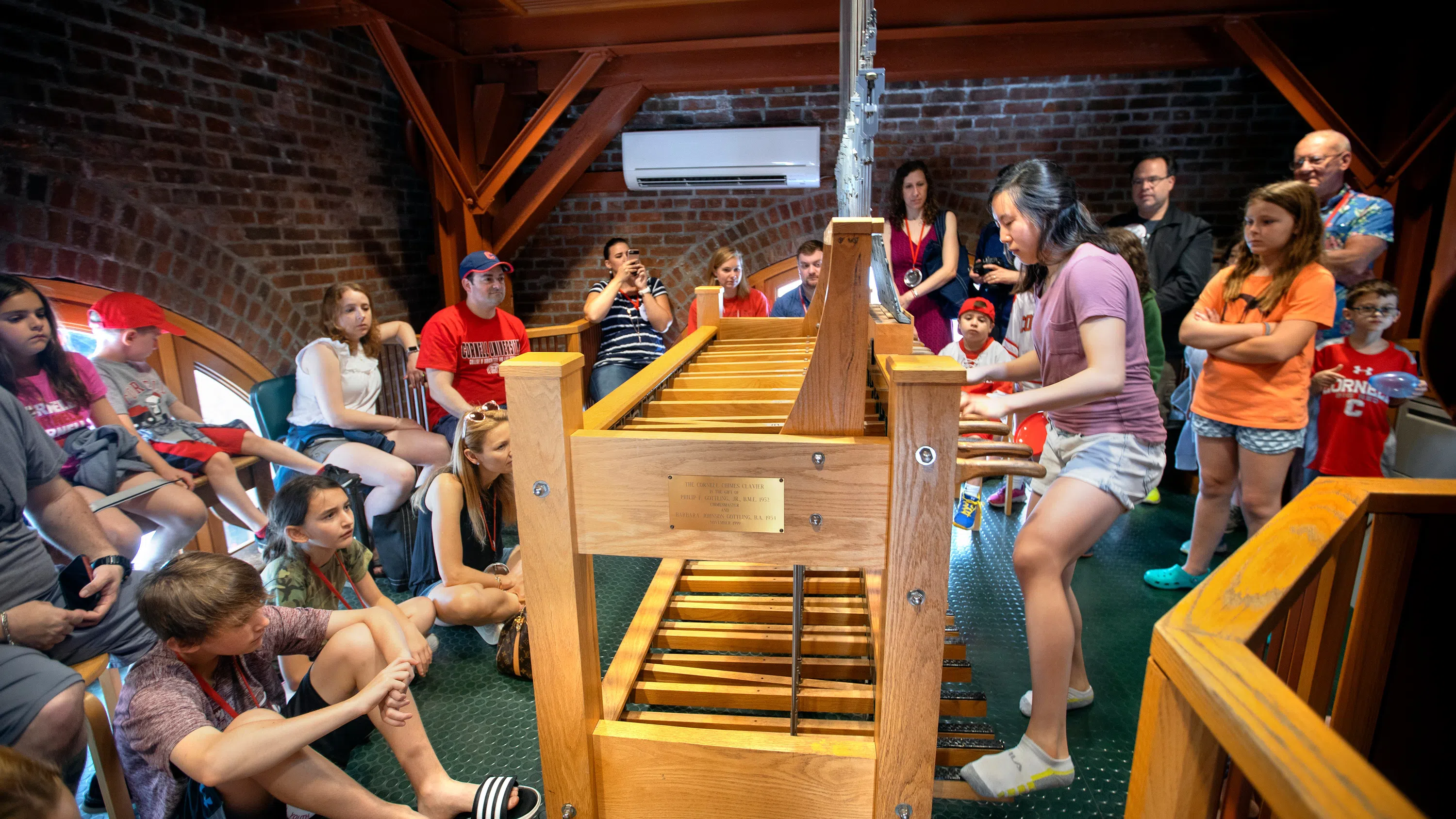 Inside the top of McGraw Tower, a chimesmaster performs on the carillon while a group of parents and students look on.