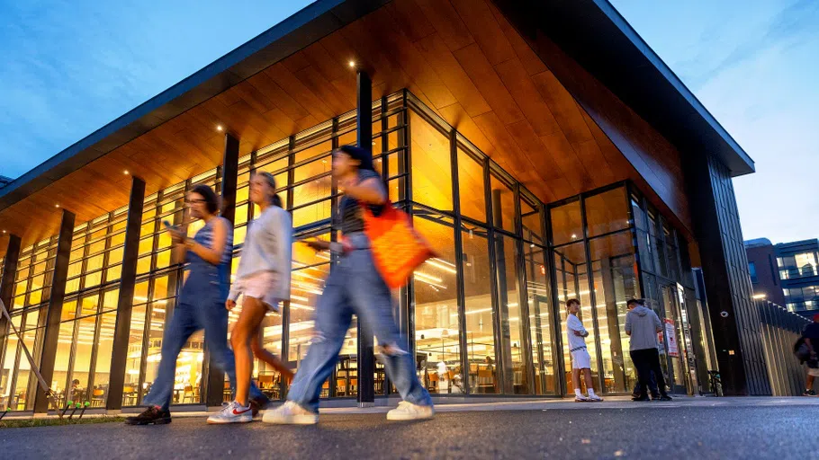 Students walk past the entrance to Morrison Dining, brightly lit in the background.