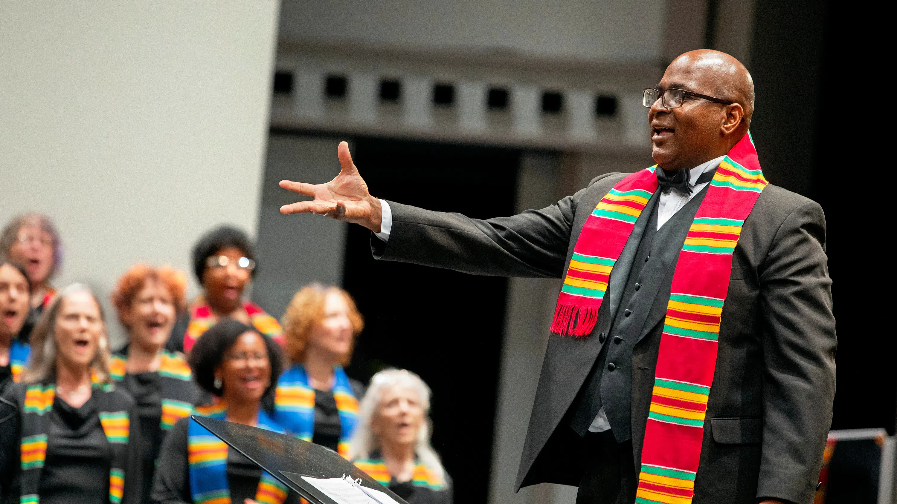 A guest conductor wearing a kente cloth stole conducts an intergenerational chorus during a tribute to civil rights pioneer Dorothy Cotton.