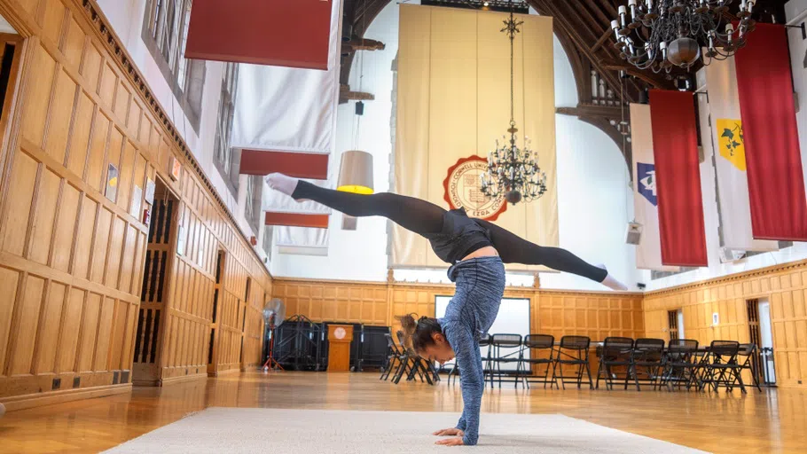 A student gymnast practices a handstand in the Willard Straight Memorial Room.